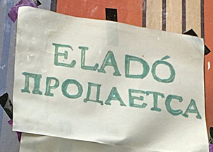 Фото 2. На окне частного дома на листе бумаги крупно написано от руки зелёными буквами венгерское слово “ELADÓ”, а под ним – русский вариант «ПРОДАЕТСЯ» с ошибкой (здесь вместо буквы «Я» используется «А»).
