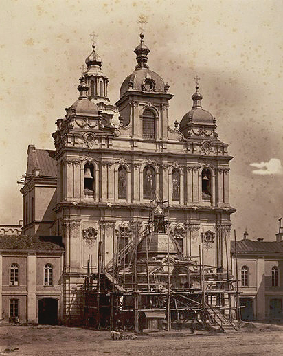 A historic baroque-style building with ornate towers and scaffolding around a central dome under restoration.

Description generated by AI